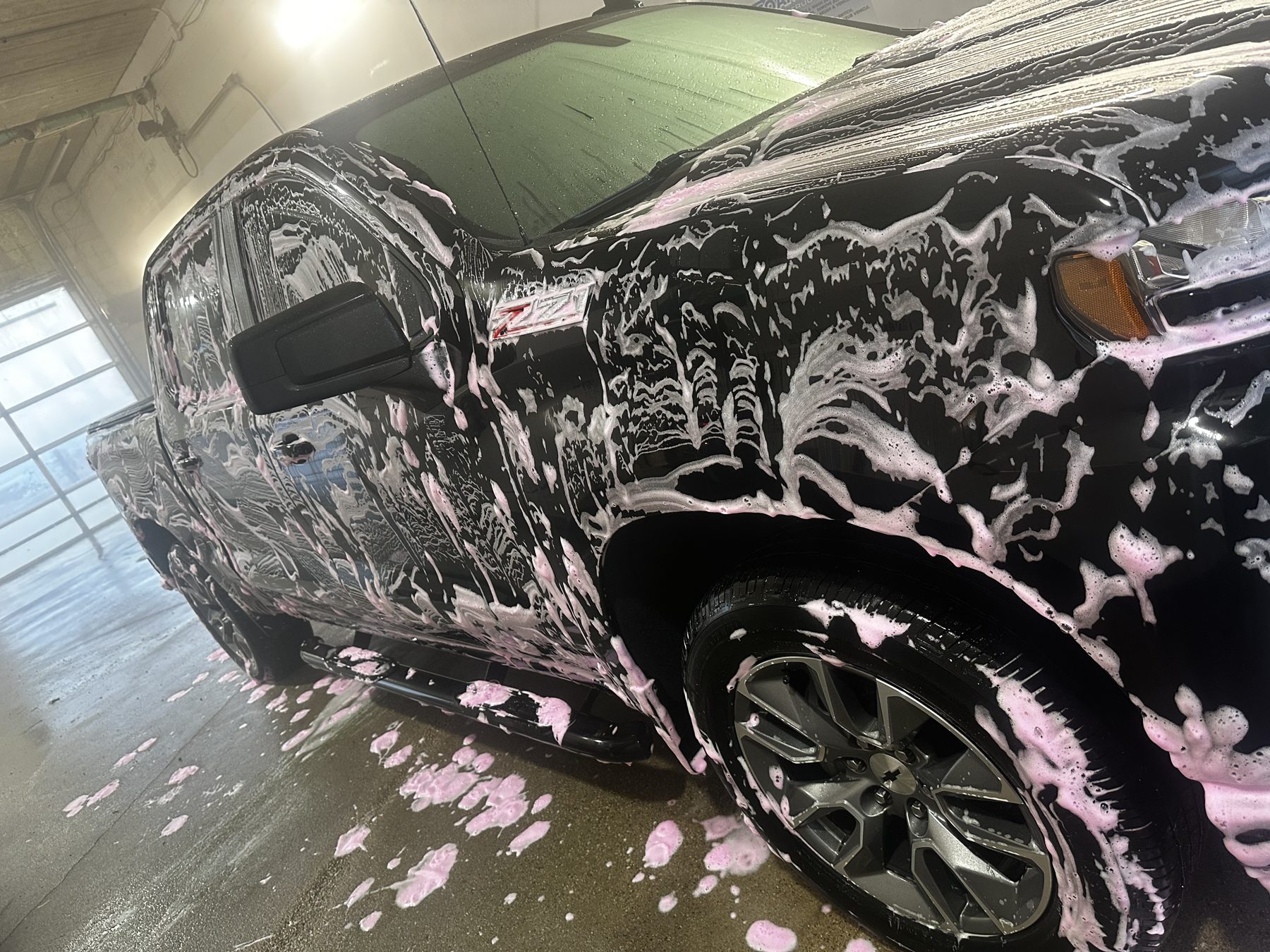 Truck covered in pink foam soap during automatic wash cycle