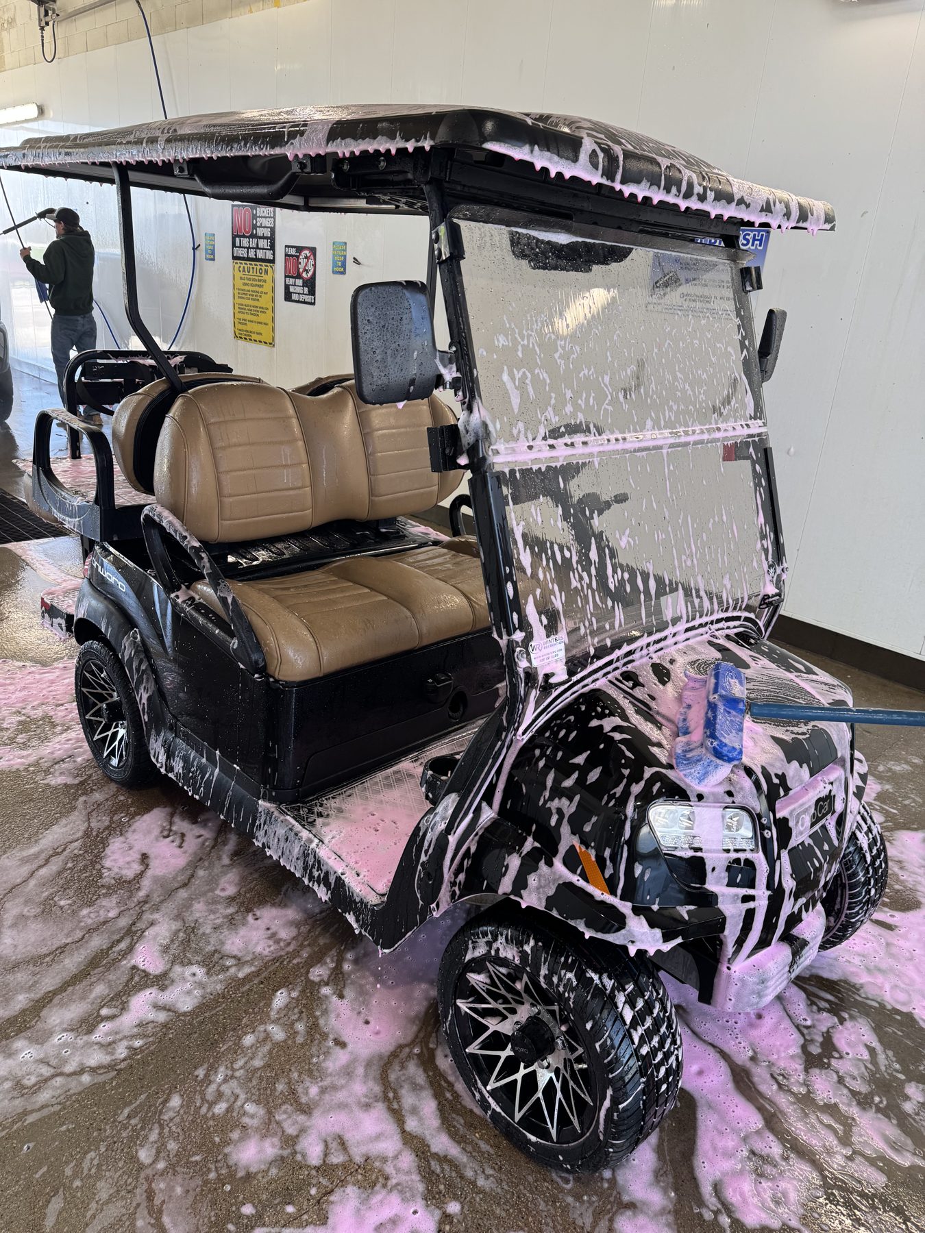 Black golf cart covered in pink foam soap during wash